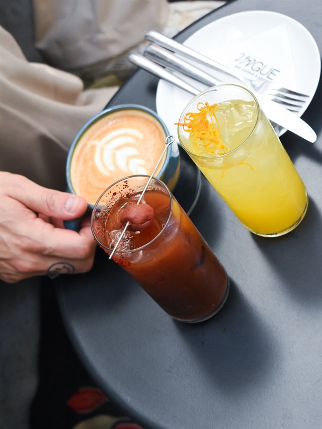 Café com leite, bloody mary e suco de laranja sobre a mesa, ao lado de um prato da casa.