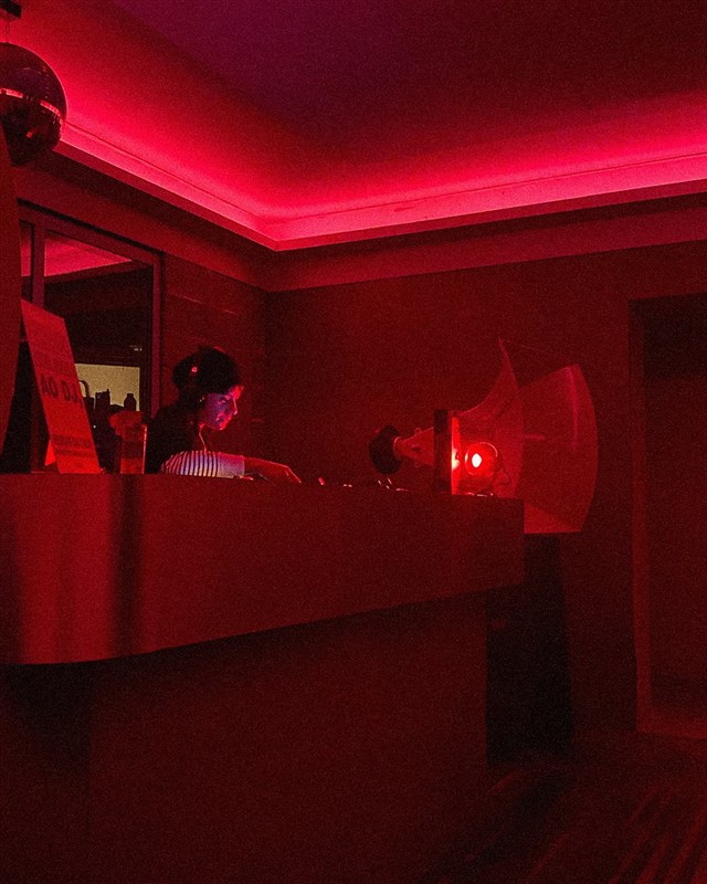 DJ na cabine sob o néon vermelho da casa.