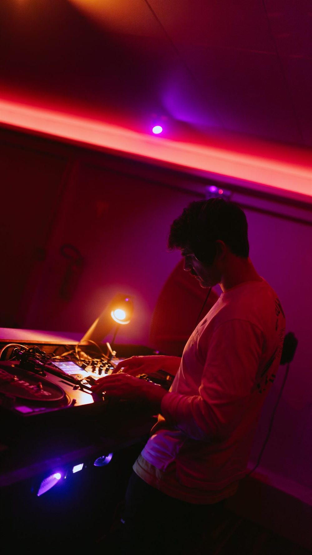 DJ selecionando discos na cabine do Vague sob a luz rosa.